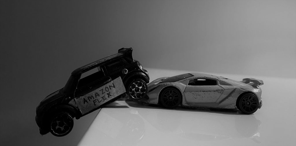 Toy car labelled Amazon Flex is pushed off the edge by a lamborghini
