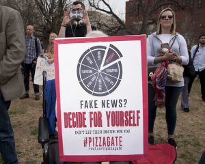Person at pizzagate gathering holding a sign that contest the idea of it being a fake news story